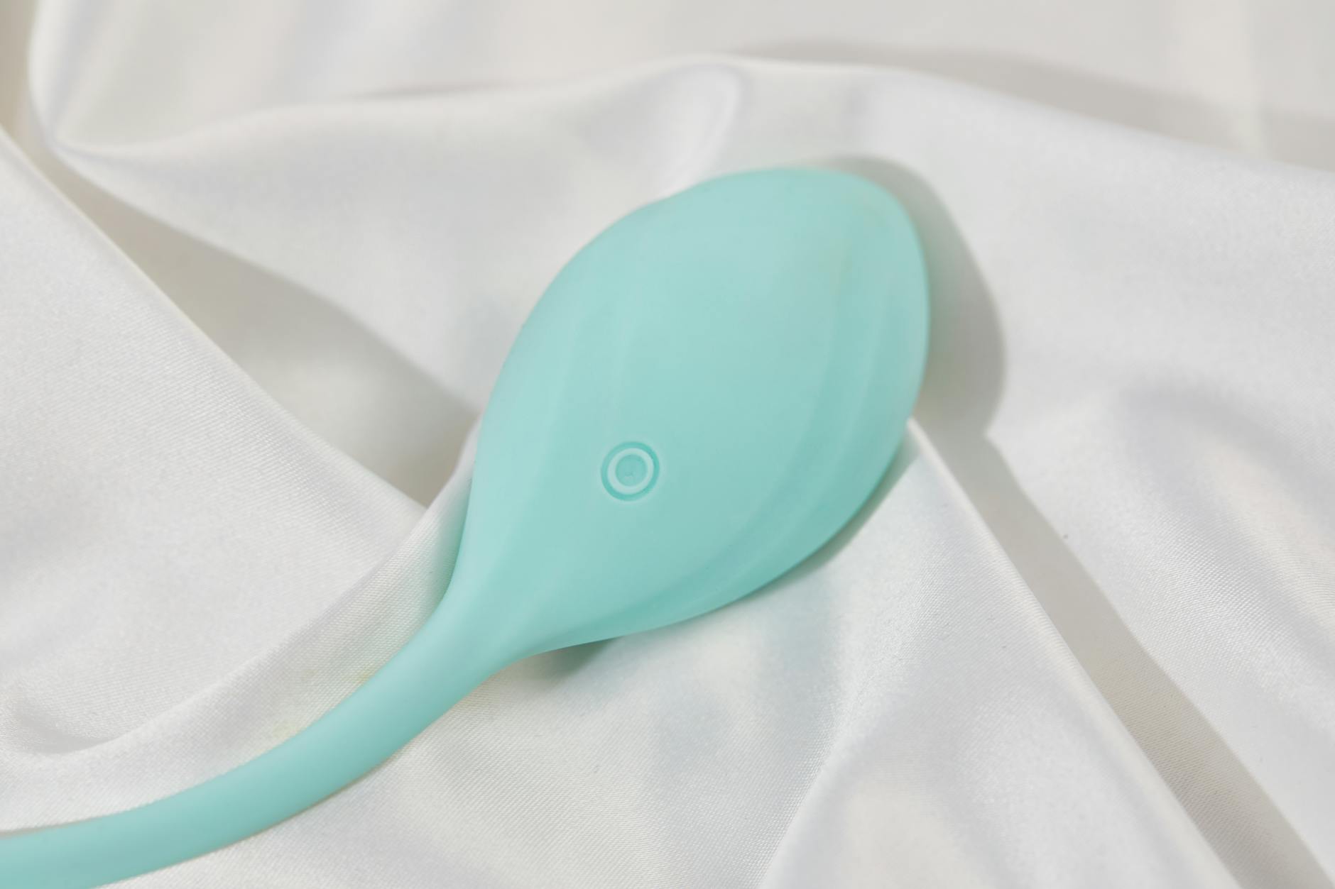 A stylish teal clitoral vibrator on smooth white silk fabric