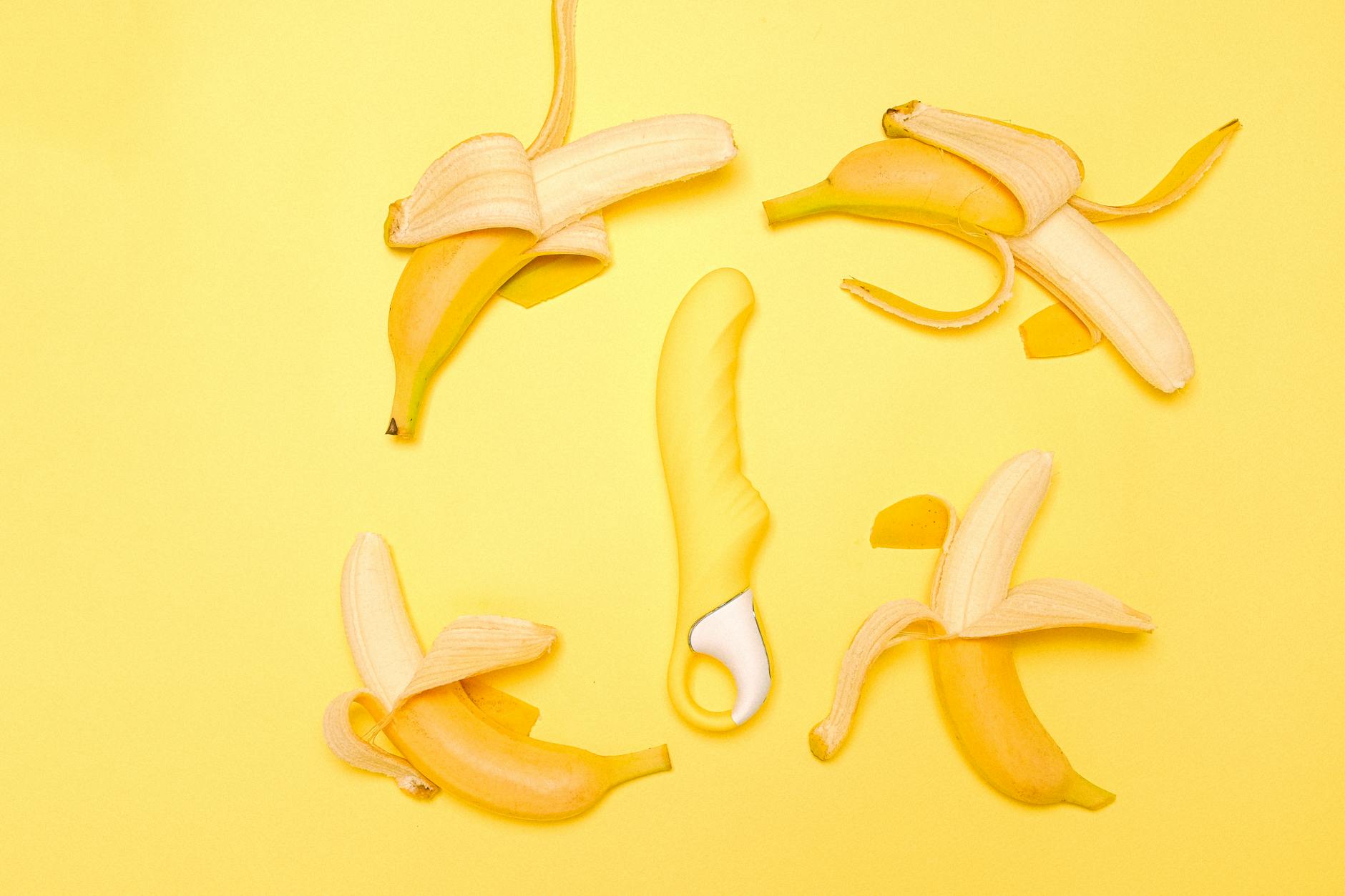 A yellow silicone clitoral vibrator surrounded by fresh lemons on a bright yellow background
