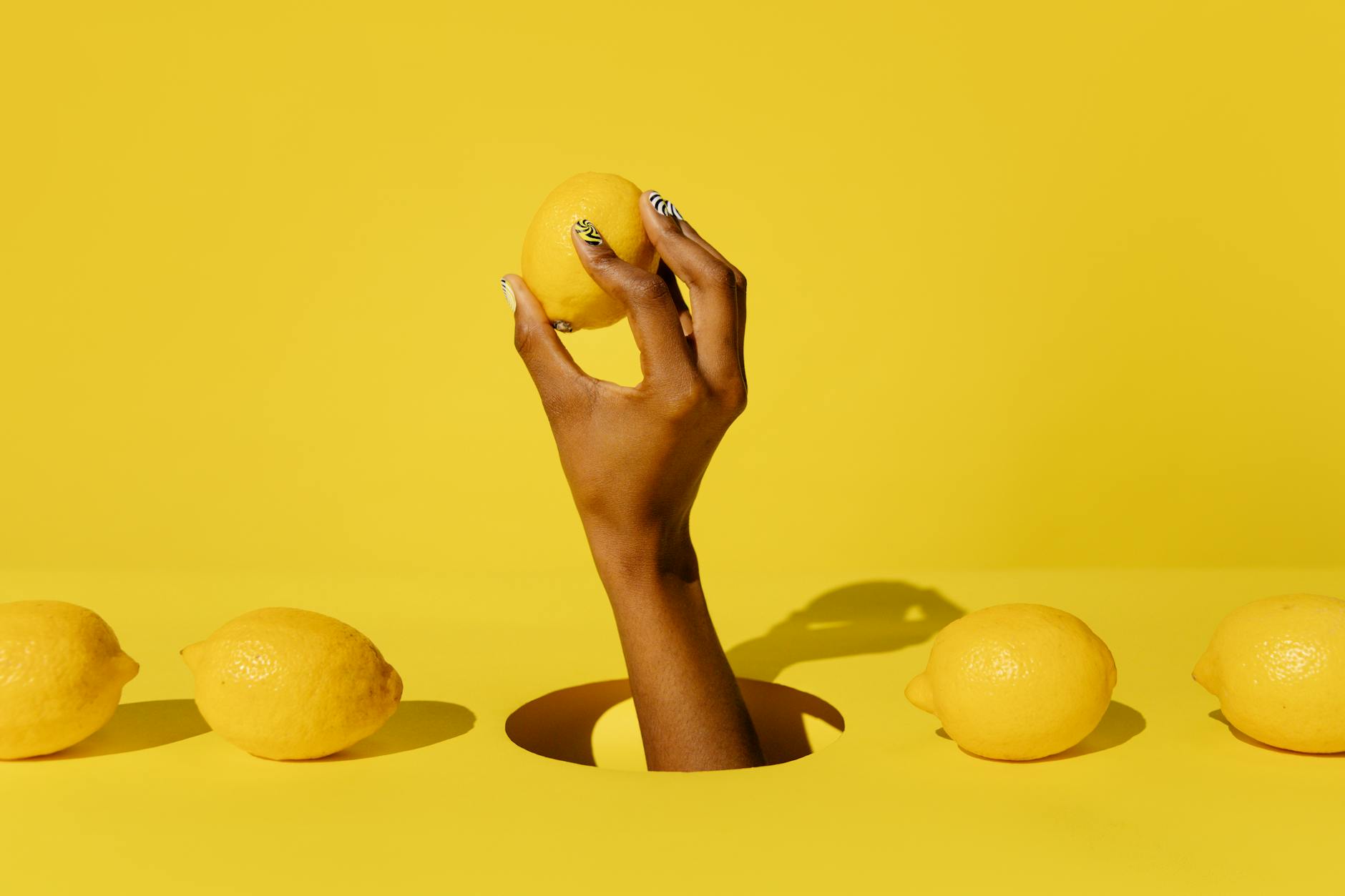Hand holding a fresh lemon against a vibrant yellow background, symbolizing the citrus design of Hellanancy Lemons clitoral vibrators