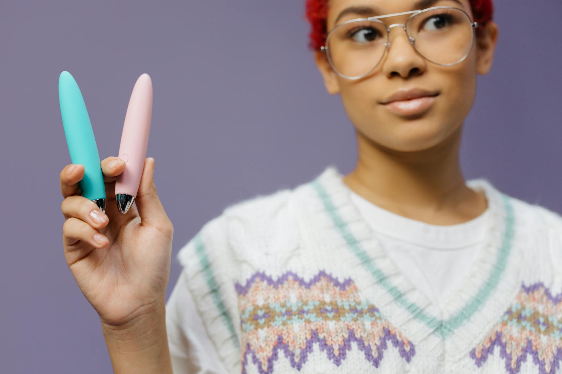 Woman holding colorful clitoral vibrators against a purple background.